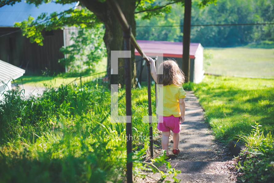 a toddler girl walking outdoors on a summer day 