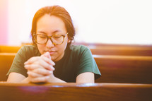 a woman praying sitting in a church pew