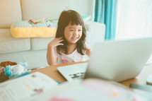 Little Asian girl with laptop computer or notebook in living rome at home