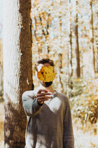 a man holding up a fall leaf in front of his face