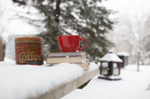 a red mug on a stack of books on a table outdoors in the snow 