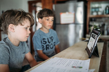 two boys doing a video conference in a kitchen 