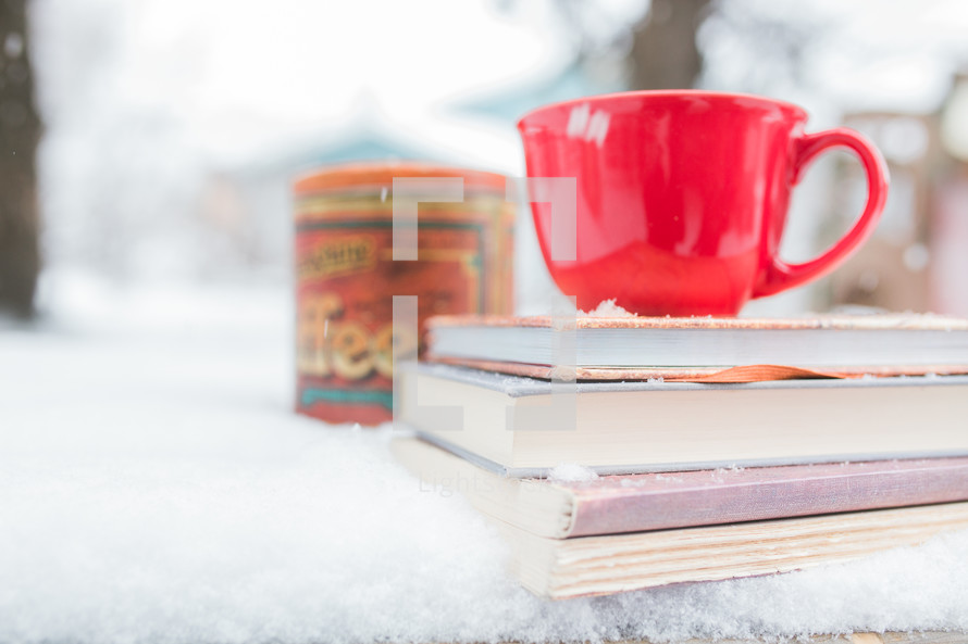a red mug on a stack of books on a table outdoors in the snow 