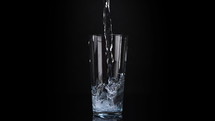 Water pouring into a glass on a black background