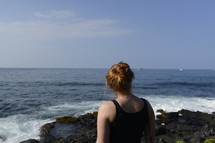 a woman standing on a rocky shore looking out over the ocean 