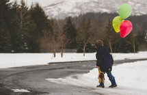 boy child walking in the snow holding a teddy bear and balloons