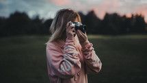 a woman with a camera taking a picture at sunset 