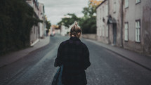 a woman walking down a street carrying a denim jacket 