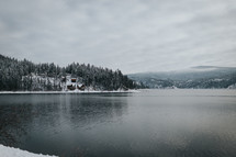 cabins on a snowy hill by a lake shore 
