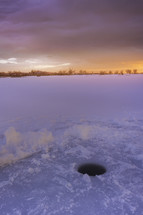 Ice fishing is a popular sport in the winter. The colorful sunrise reflects on the frozen lake