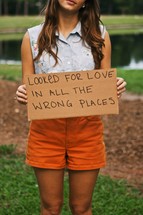 woman holding sign with the words LOOKED FOR LOVE IN ALL THE WRONG PLACES