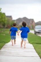 Two little boys running down a sidewalk