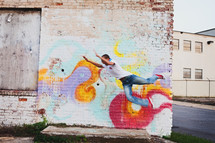 man jumping in front of a painted brick wall