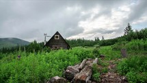 Grey clouds moving over small mountains hut in green wilderness nature Time lapse