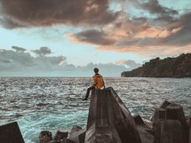 boy sitting on a rock looking out at the ocean 