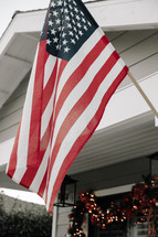 An American flag hanging above a front porch decorated for Christmas.