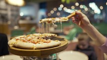 Close-up of hand taking slices of pizza from wooden board. People eat fast food in cafe.