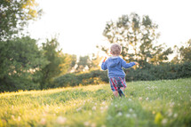 A little boy running through a field of green grass.