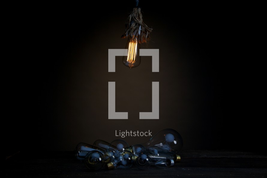 An illuminated lightbulb shining on a pile of unlit bulbs