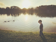 a toddler boy walking by a pond 