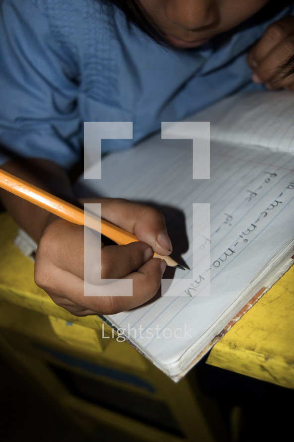 Child writing on notebook paper in a classroom in Honduras