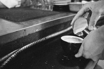 A barista pouring cream into a coffee mug