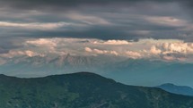 Gray clouds moving over alpine mountains in summer evening landscape; time lapse.
