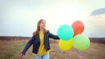 Cheerful girl holding balloons running on meadow
