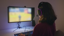 Teenage girl sitting in front of a computer, playing a game wearing a headset