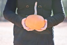torso of a woman holding a pumpkin