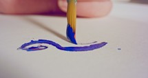 Macro shot of someone painting on paper with blue acrylic paint.