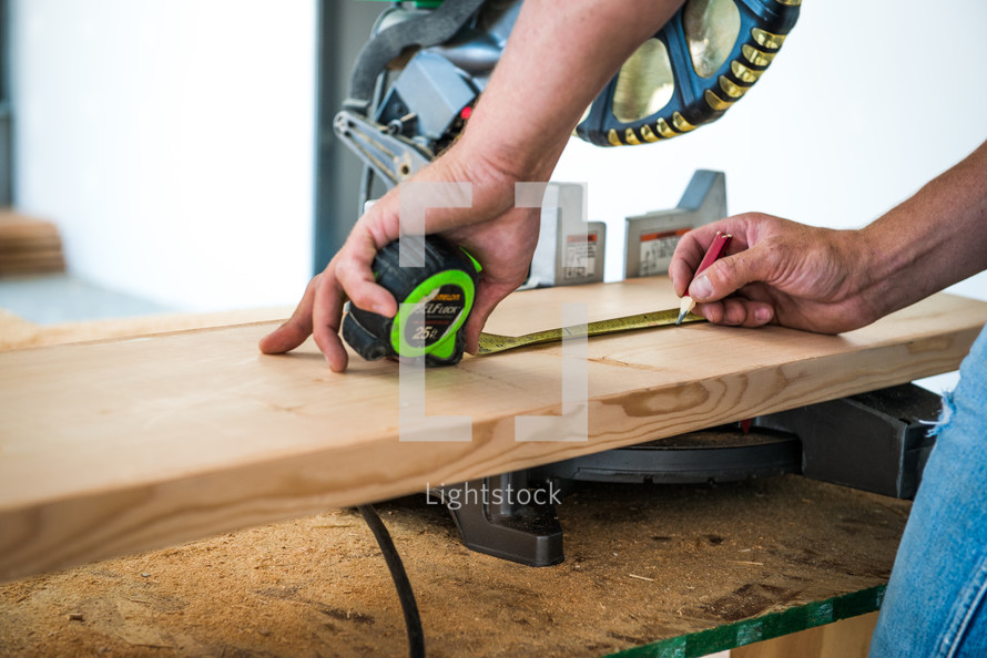 Man holding a measuring tape over a piece of wood under a chop saw.