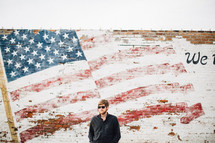 man standing in front of an American Flag painted on a brick wall 