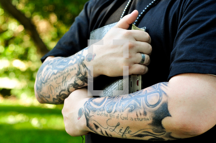 man with But the gift of God is eternal tattooed on his arm holding a Bible