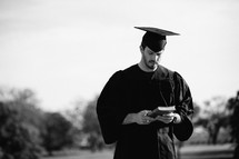 Graduate standing outdoors holding a Bible.