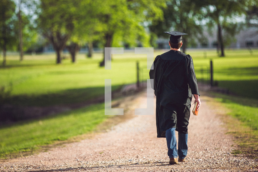 Graduate walking on dirt road holding a Bible.