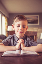 boy child with praying hands over the pages of a Bible 