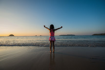 a girl standing on a tropical beach with arms raised 