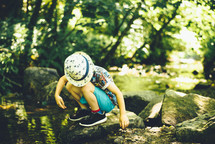 a boy playing with rocks by a stream 