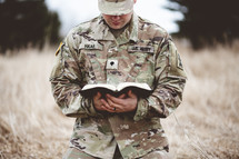 Christian soldier kneeling in a field praying holding a Bible 