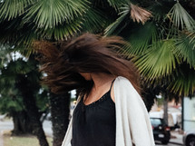 a woman flipping her hair under palm trees 