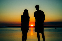 Silhouette of a couple standing on the beach at the ocean at sunset.