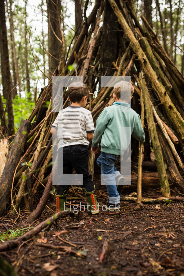 boys and a teepee of sticks in the woods 