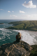 a woman sitting on the edge of a cliff taking in the views of the ocean In New Zealand 