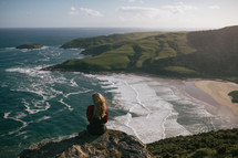 a woman sitting at the edge of a cliff in New Zealand 