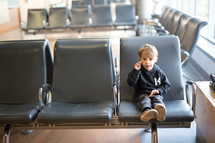 a boy child in a waiting area playing on a cellphone 