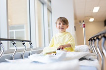 a boy child in a hospital gown playing with toy cars  in a hospital bed 
