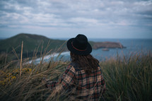 a man in a plaid shirt and hat sitting at the top of a mountain along the shores of New Zealand 