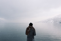 a woman standing on a lake shore with snow in her hair 