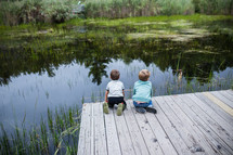 children looking at pond water from a dock 